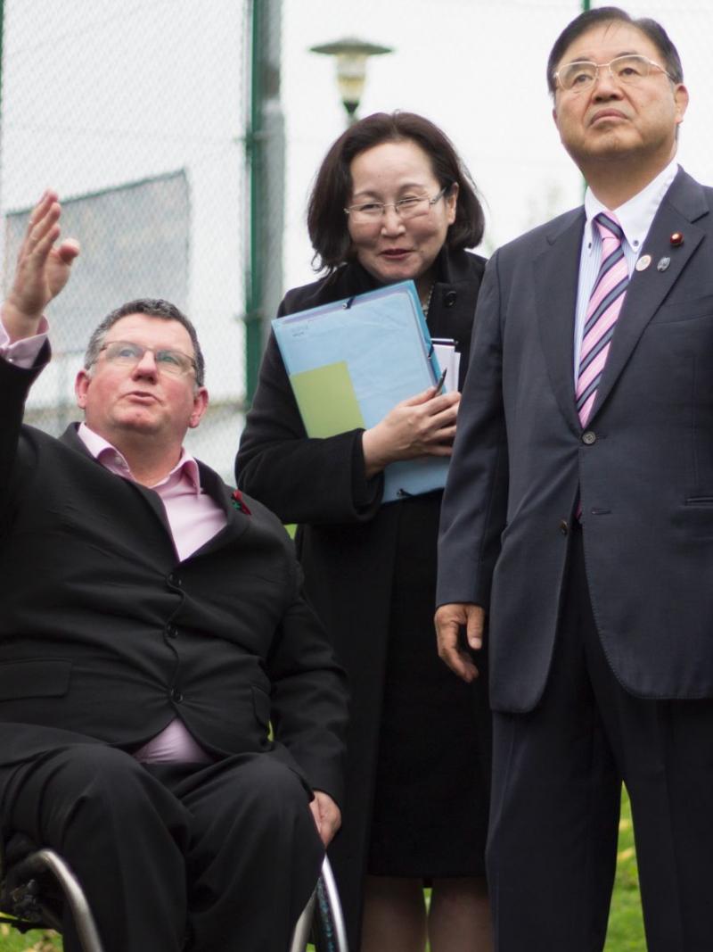 Man in wheelchair points at something, shows something to a man and woman.