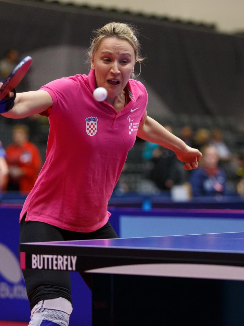 the upper body of a female playing table tennis and wearing a pink polo shirt