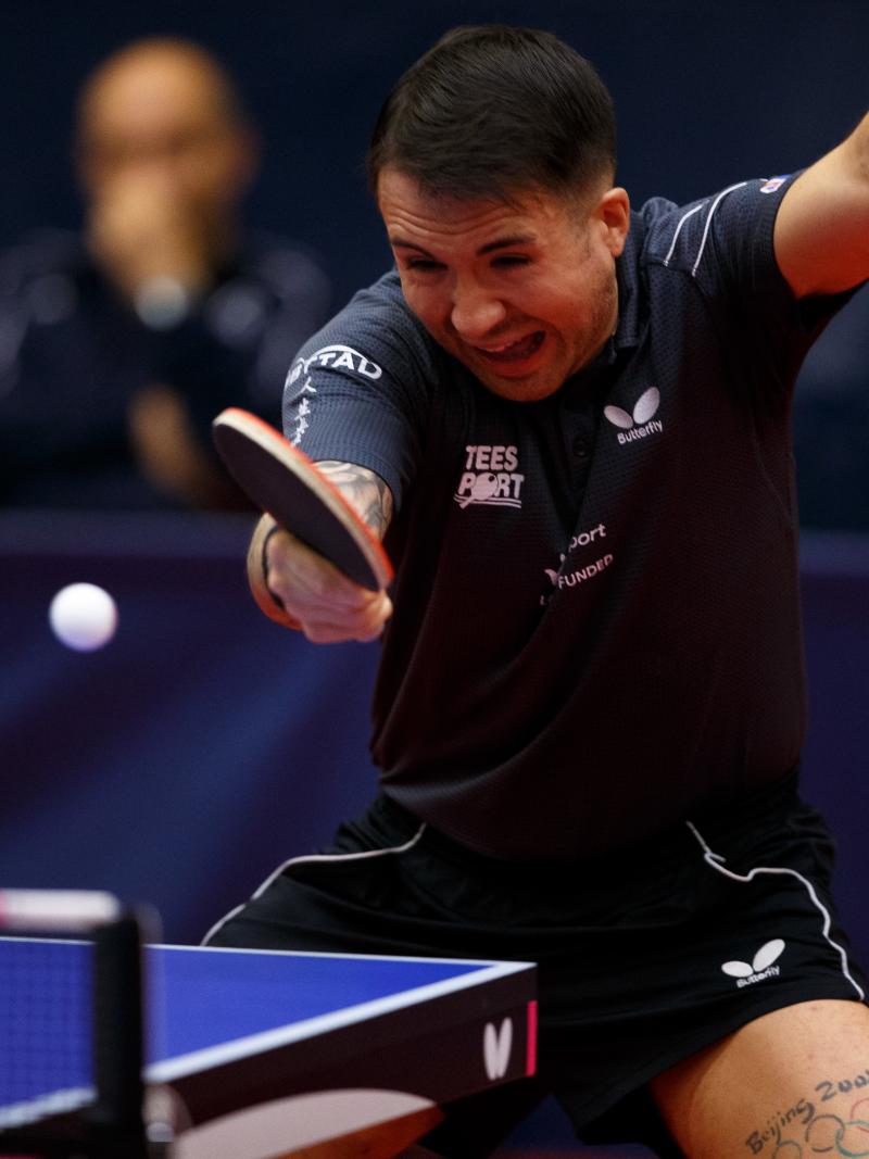 A man wearing a navy shirt playing table tennis