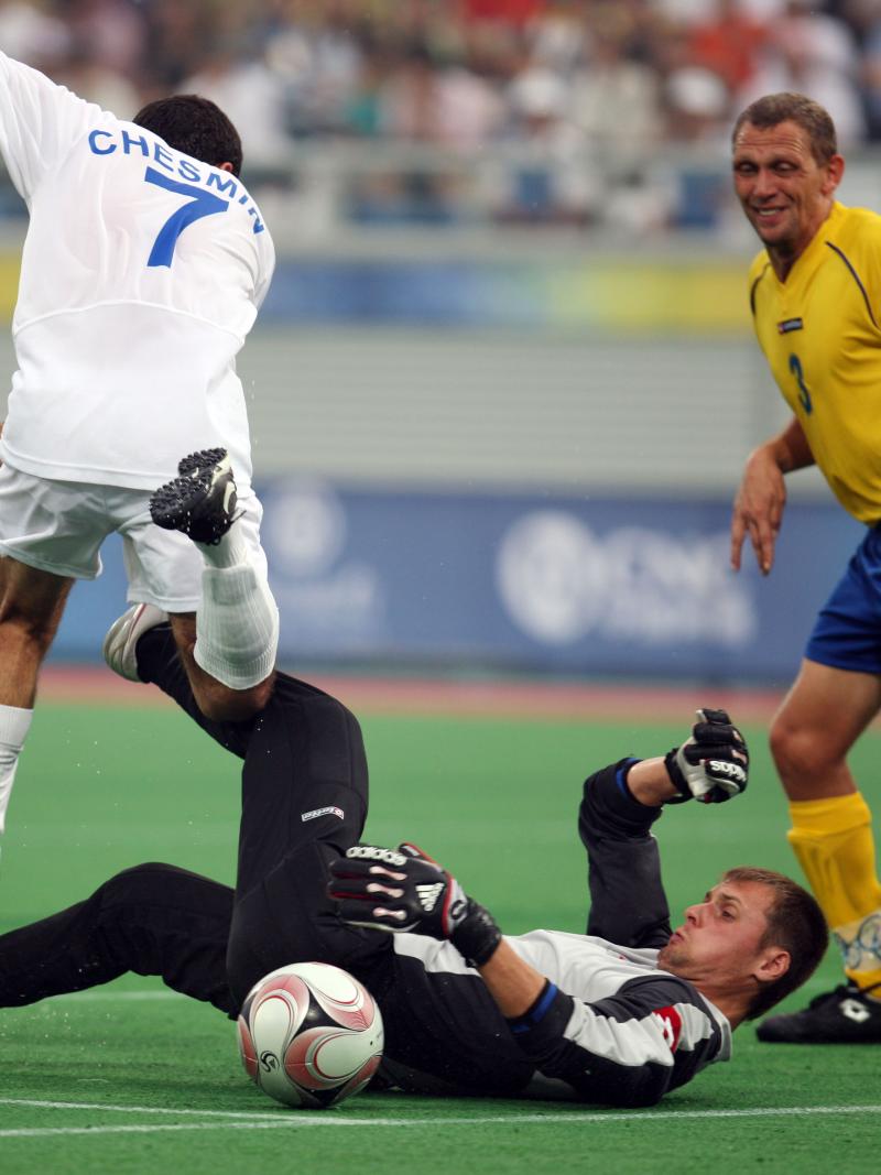 Man on the ground. other man jumping over him. Both focusing on a ball