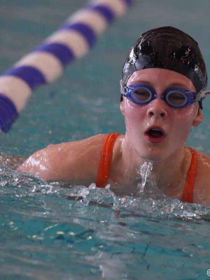 Girl swimming in the pool with swimcap and goggles on.