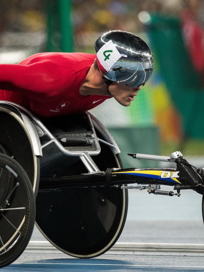 Close up of a wheelchair racer with a red racing suit and a silver helmet.