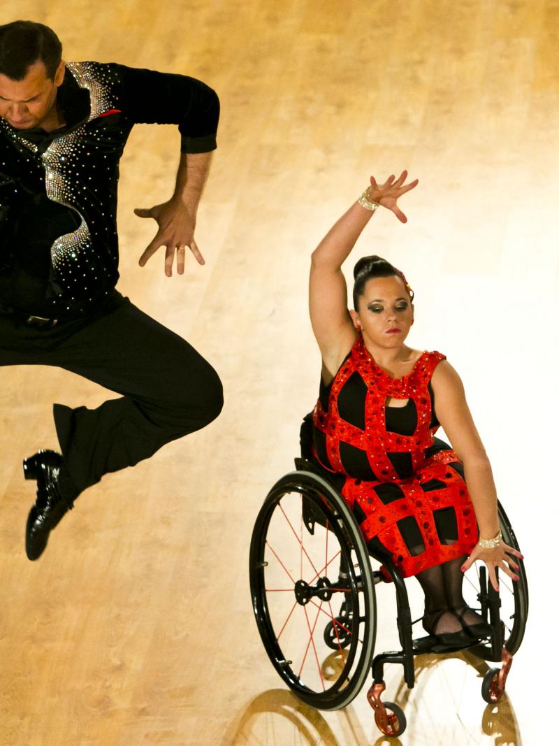 A woman in wheelchair dances with her stand-up partner who is jumping