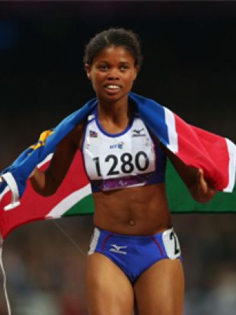 A picture of a woman running with a Namibian flag on her shoulder 