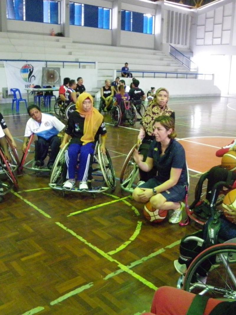 A coach kneels while women in wheelchairs gather around her