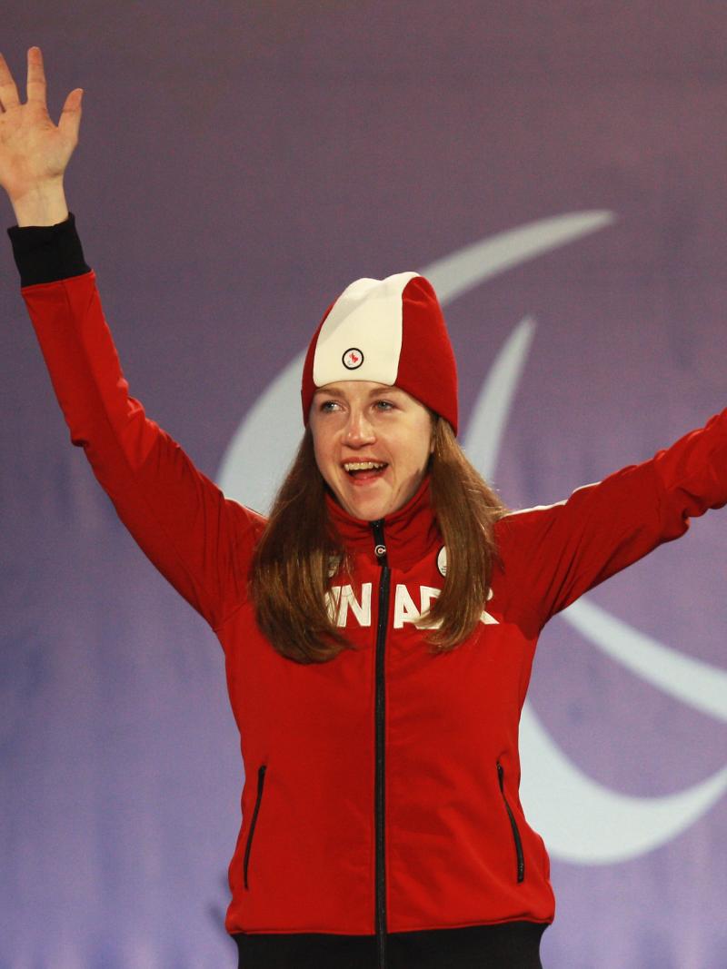 a female Para skier raises her arms in celebration on the podium