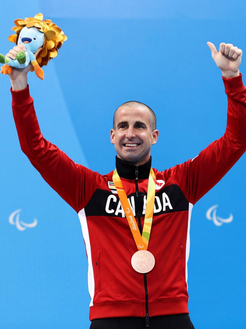 a male Para swimmer raises his arms on the podium