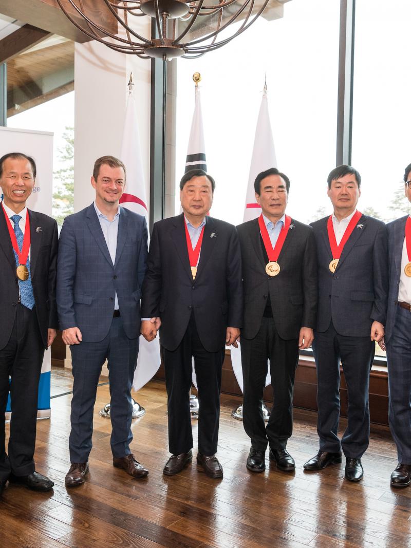 Eight men standing, six of them with the Paralympic Order medal