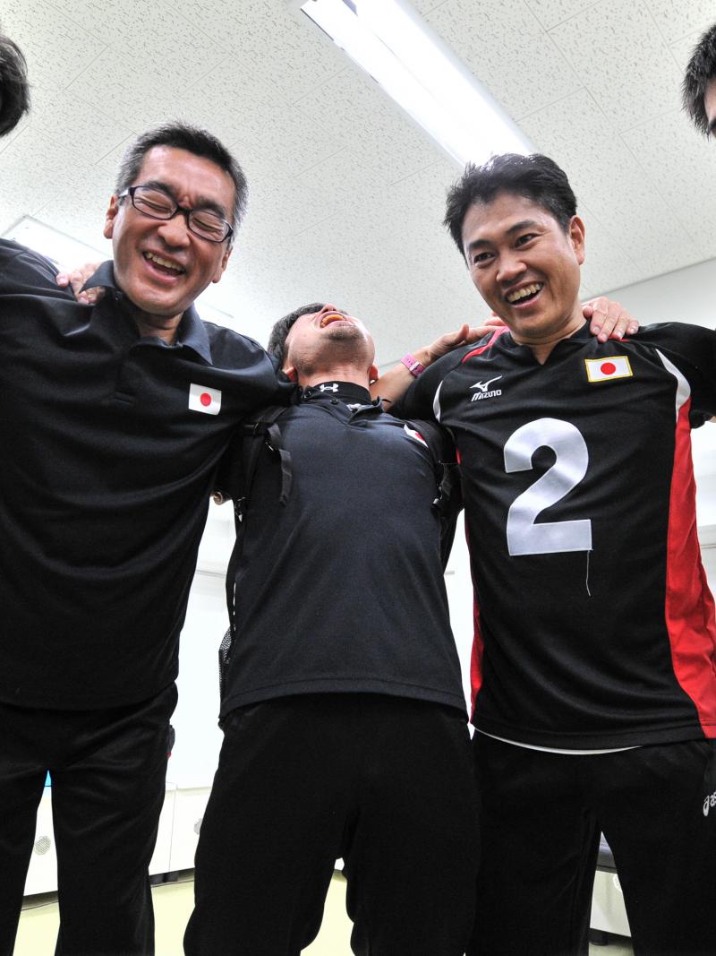 a group of male goalball players standing in a circle laughing 