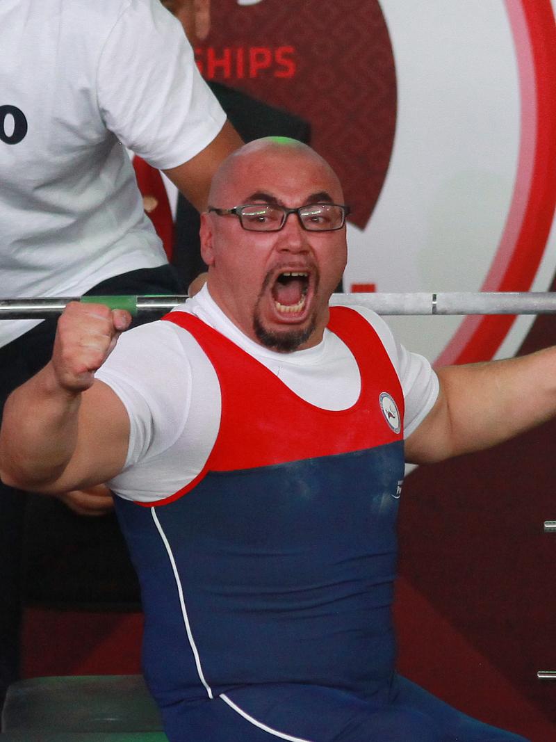 a male powerlifter raises his fists in celebration on the bench