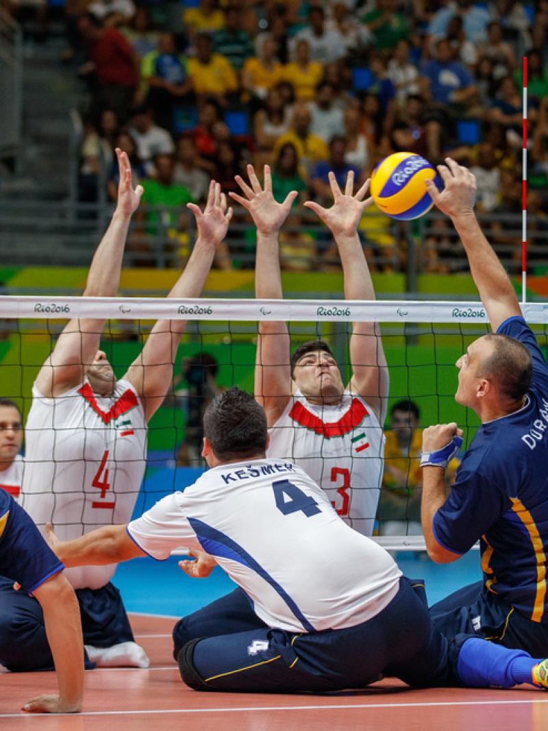 a group of male sitting volleyball players in action on the court