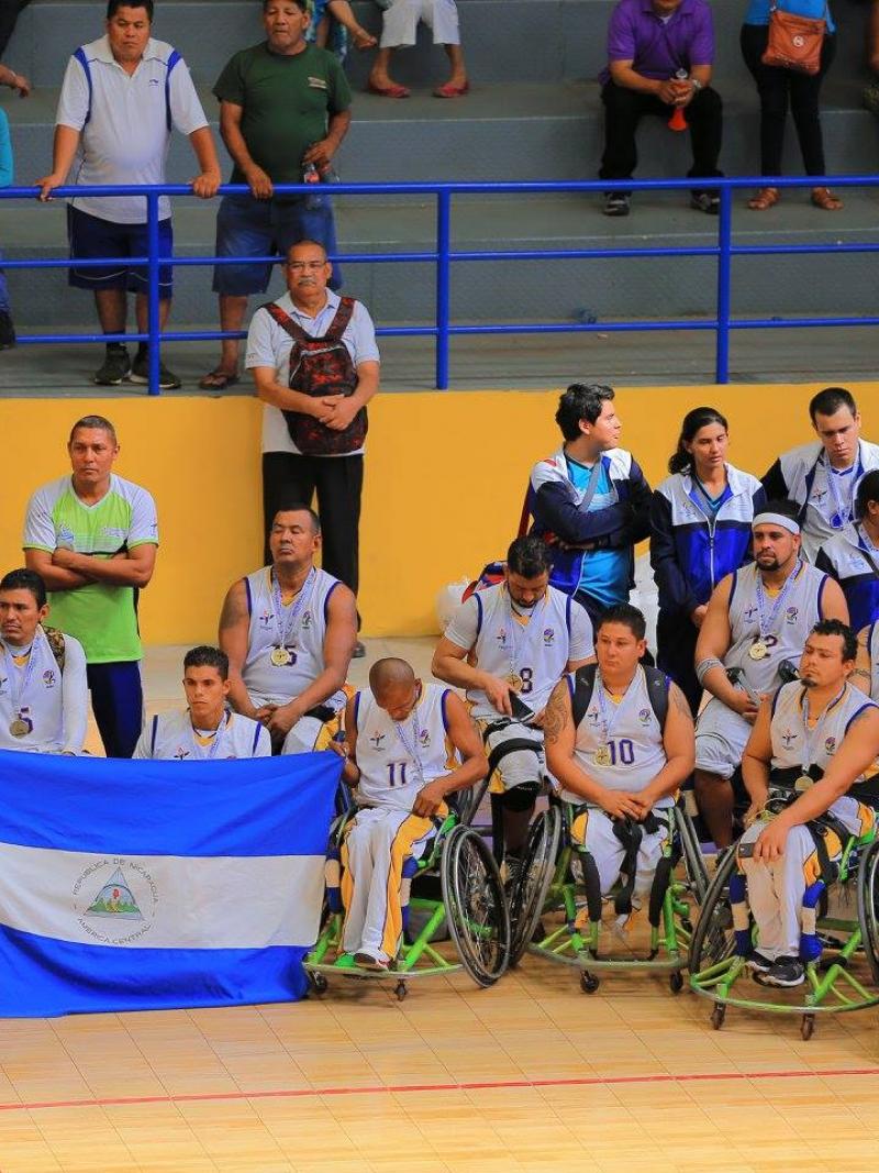 Nicaragua's wheelchair basketball players on a court holding up the Nicaragua flag