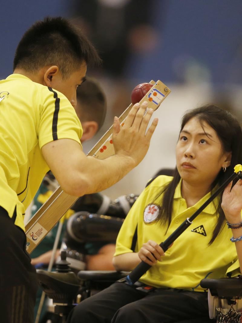 female boccia player Ho Yuen Kei listens to her coach before taking a shot