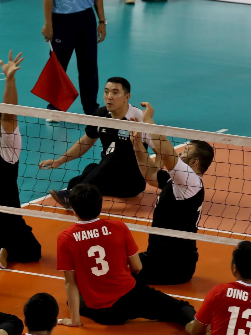 male sitting volleyball players from China and Kazakhstan volleying the ball over the net