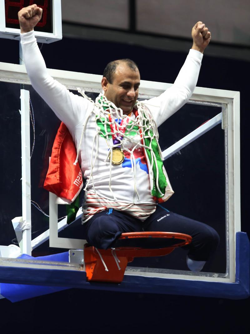 male wheelchair basketball player Morteza Ebrahimi sitting on top of the basketball hoop raising his arms