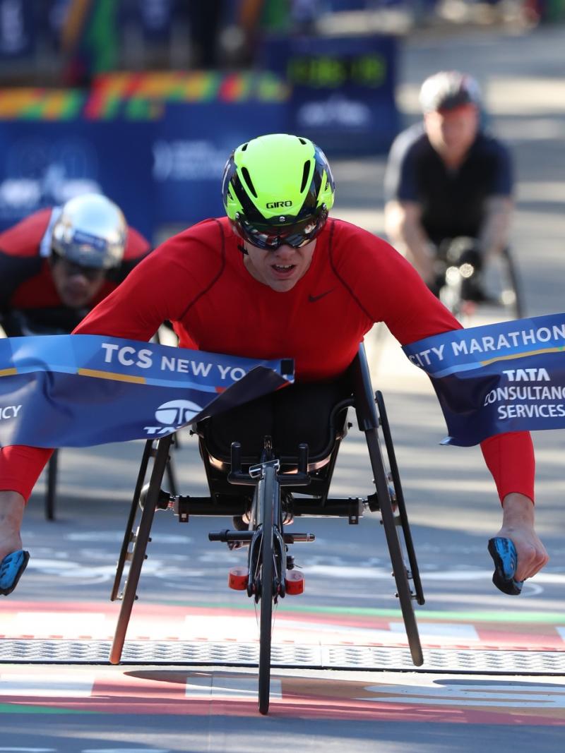 male wheelchair racer Daniel Romanchuk breaks the tape on the finish line ahead of two other wheelchair racers