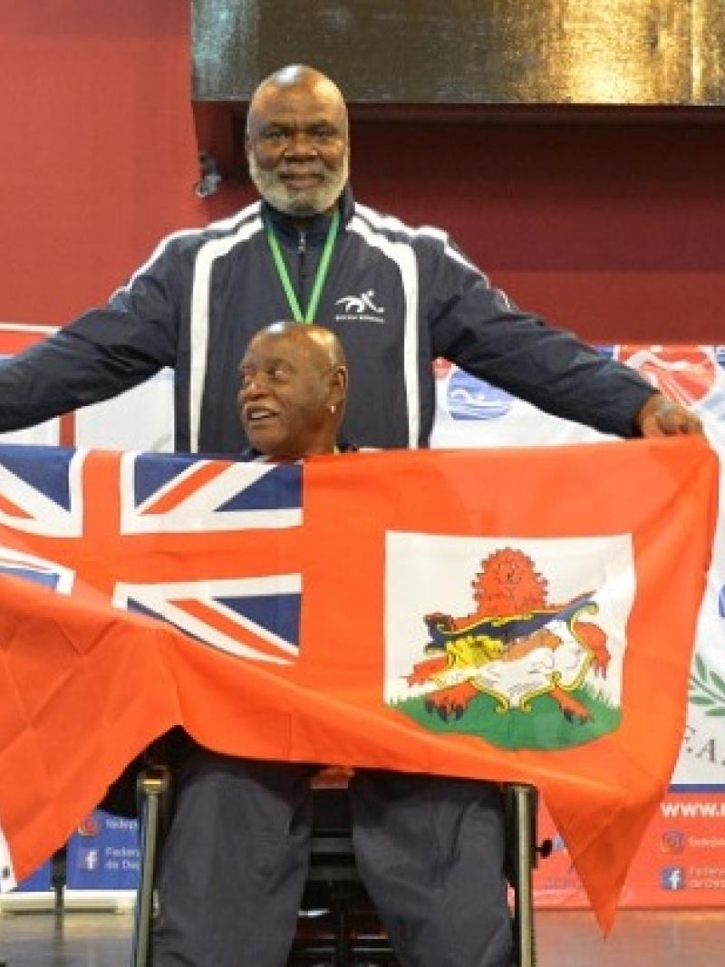 male boccia athlete Steve Wilson on the podium holding up a Bermuda flag