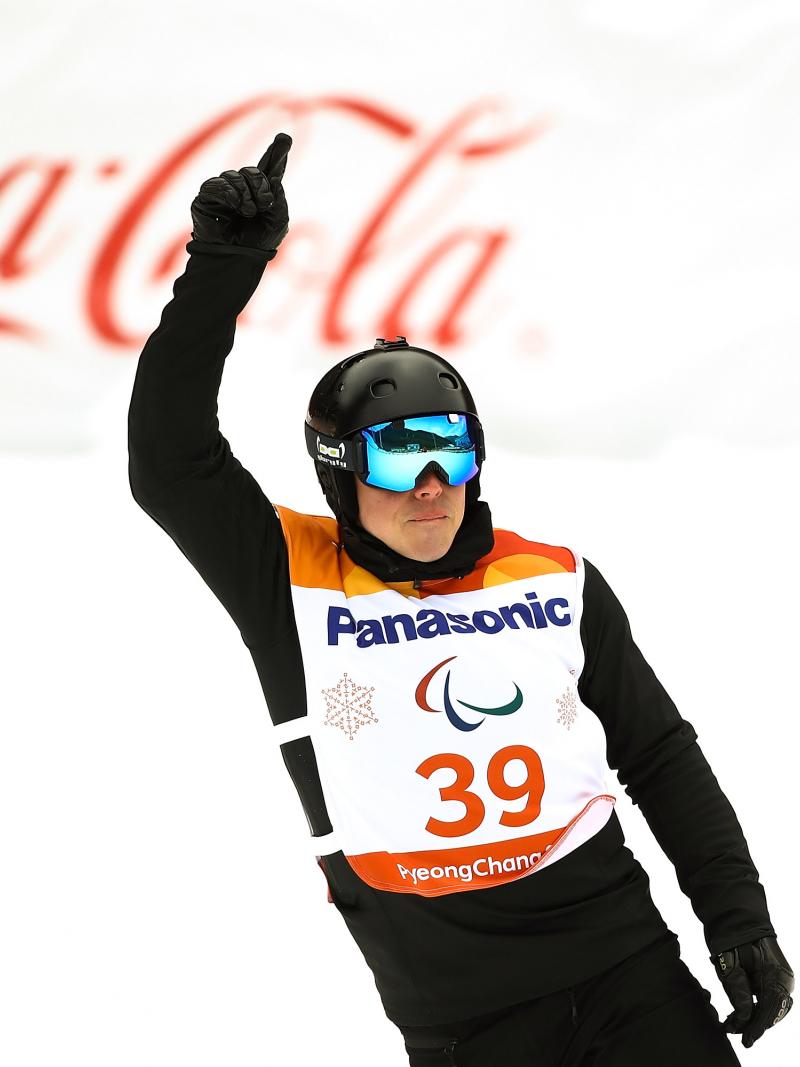 male Para snowboarder Matti Suur-Hamari raises his finger as he crosses the finish line