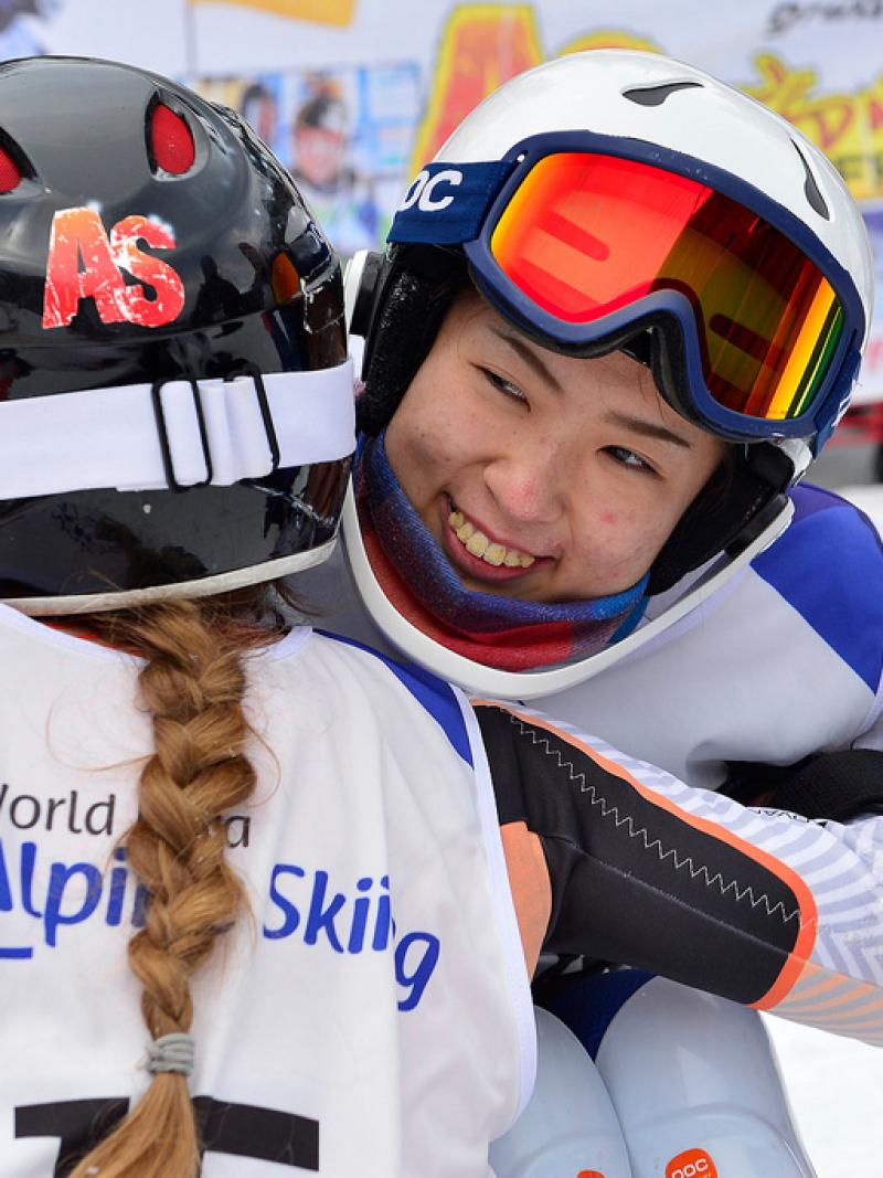 female Para alpine skier Momoka Muraoka hugs another female skier and smiles
