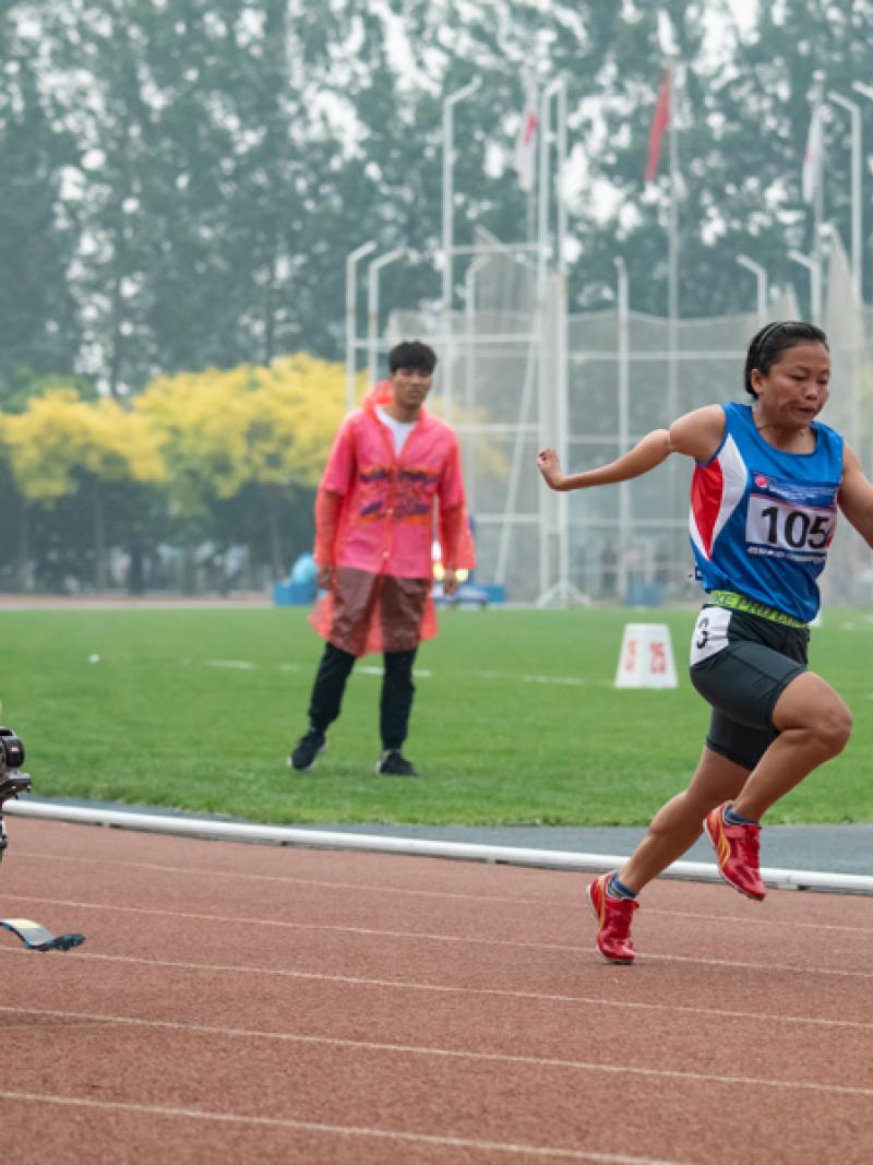 A double-leg amputee woman running against another woman on an athletics track