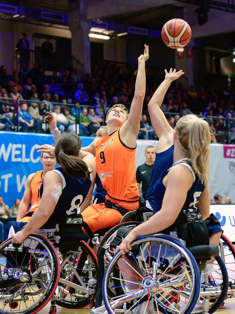 female wheelchair basketball players from Netherlands and Great Britain reaching up for the ball