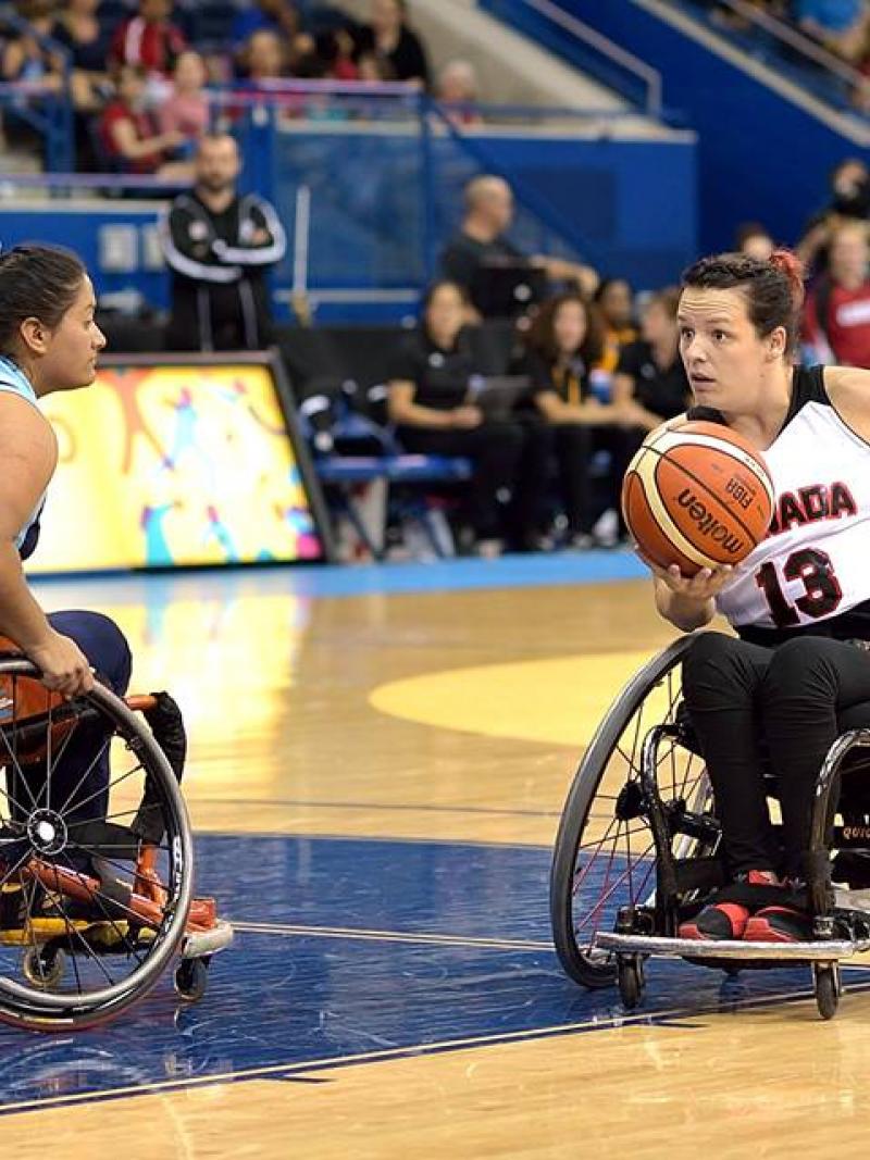 Canadian wheelchair basketball player holds the ball as an Argentinian defender tries to prevent her from scoring