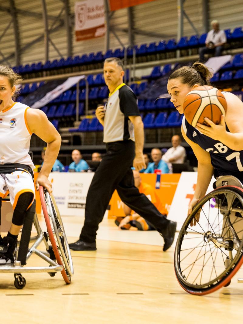 British female wheelchair basketball player makes a move with the ball while a Dutch player turns to defend her