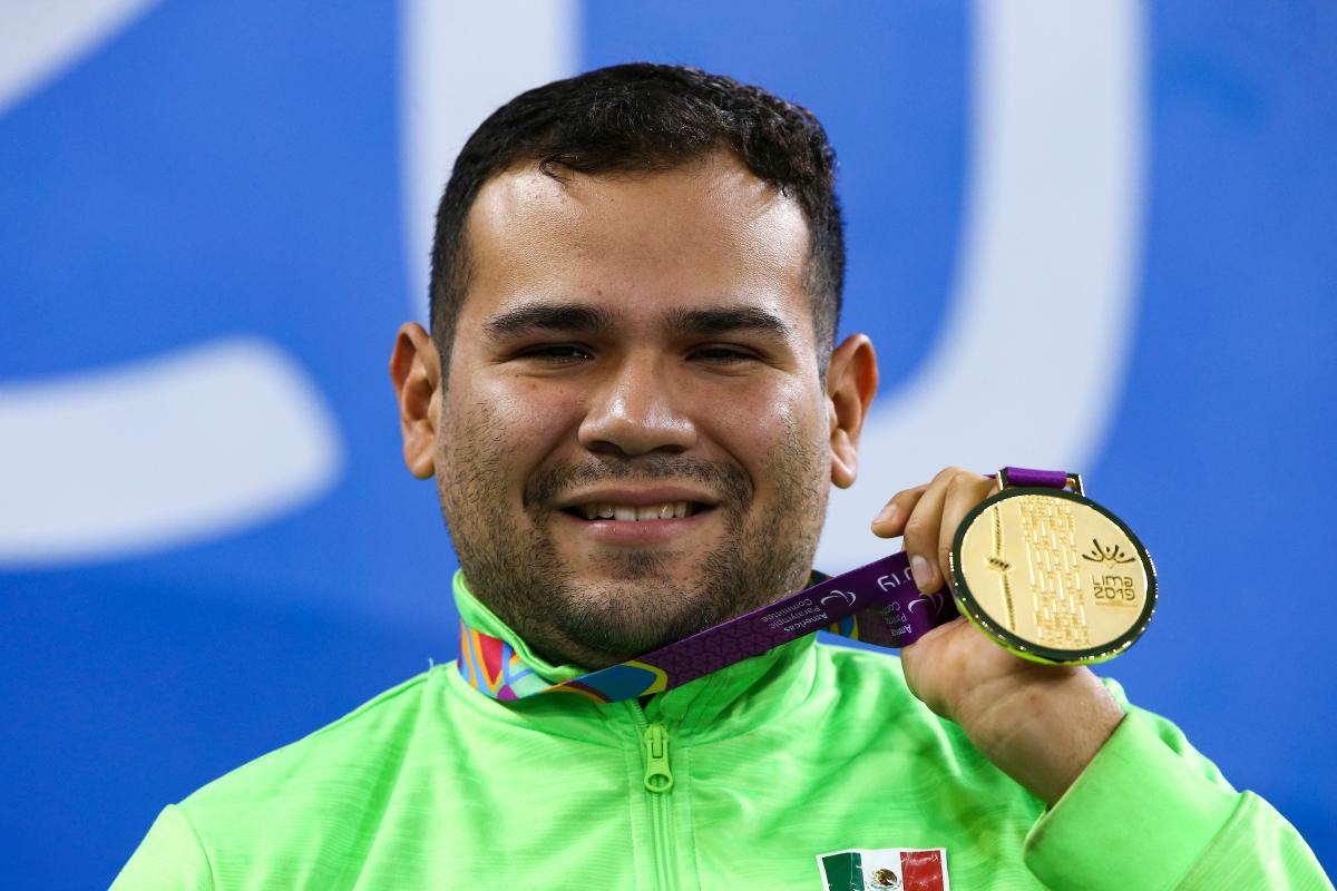 a male Para swimmer holds up his gold medal