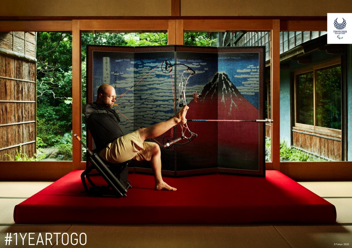 Armless archer sits down holding bow and arrow with foot with Japanese backdrop