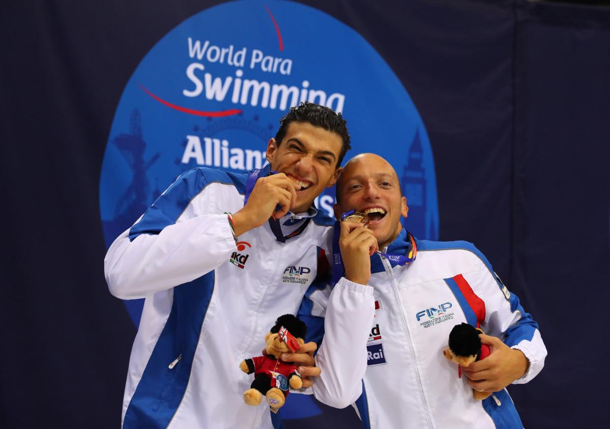 two male Para swimmers biting their medals