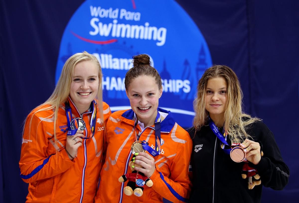 three female Para swimmers on the podium holding up their medals