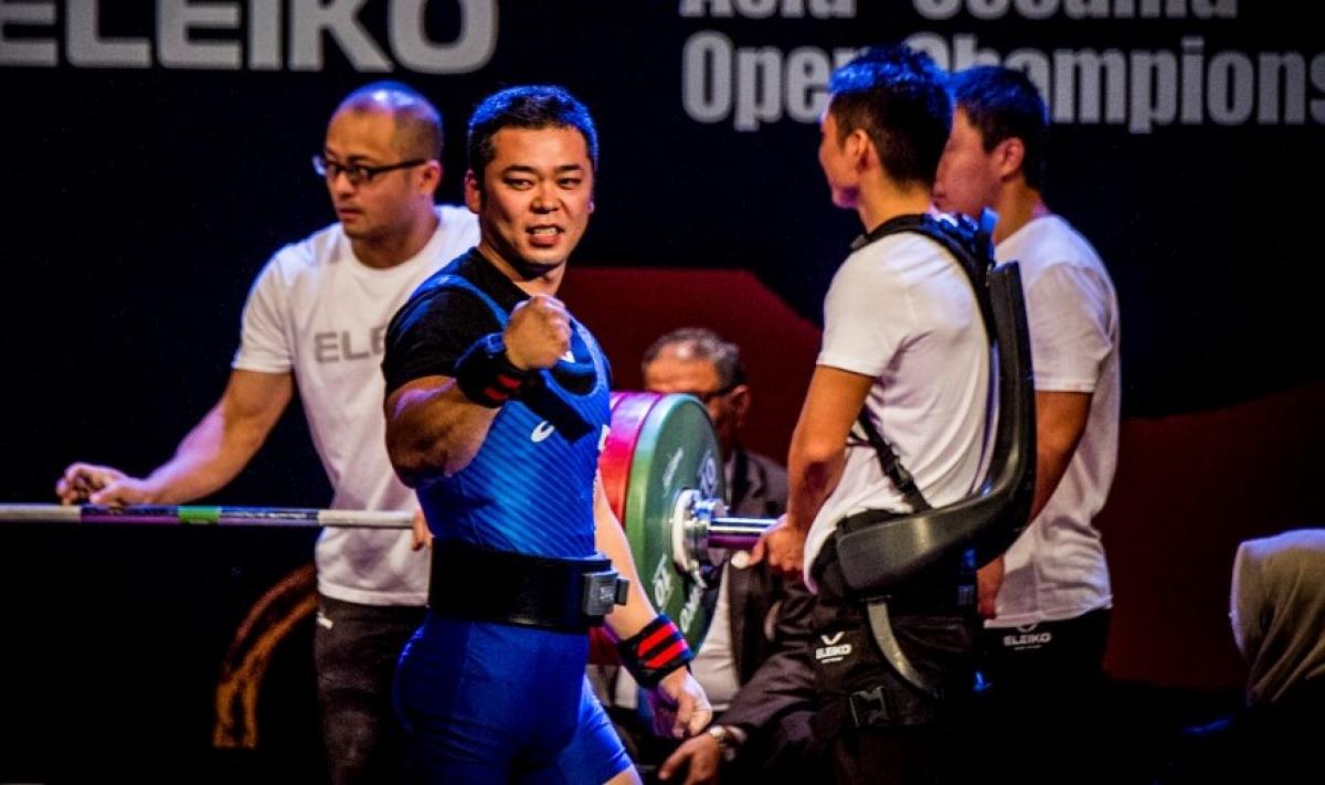 A male Para powerlifter celebrating with three assistants in the background