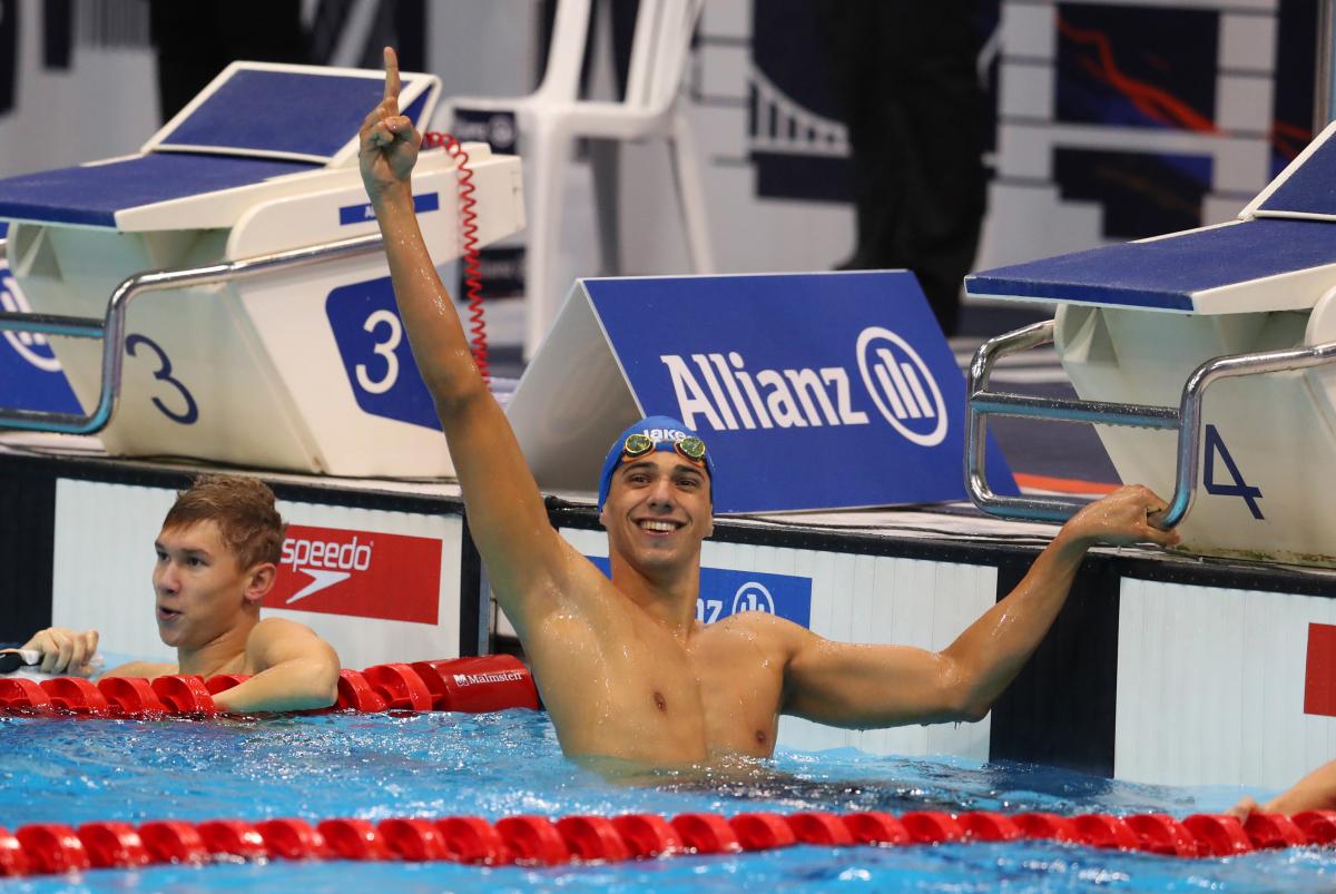 a male Para swimmer raises his arm in celebration in the pool