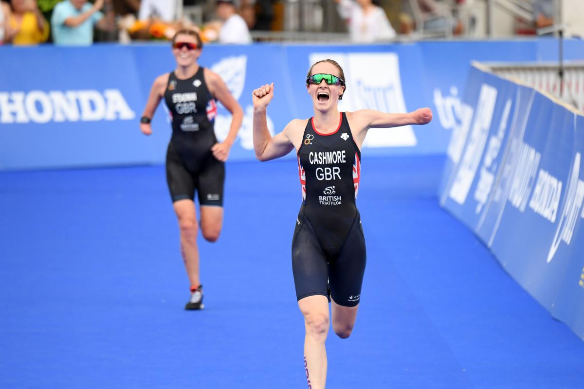 Female triathlete with arm amputation celebrates with opponent in background smiling