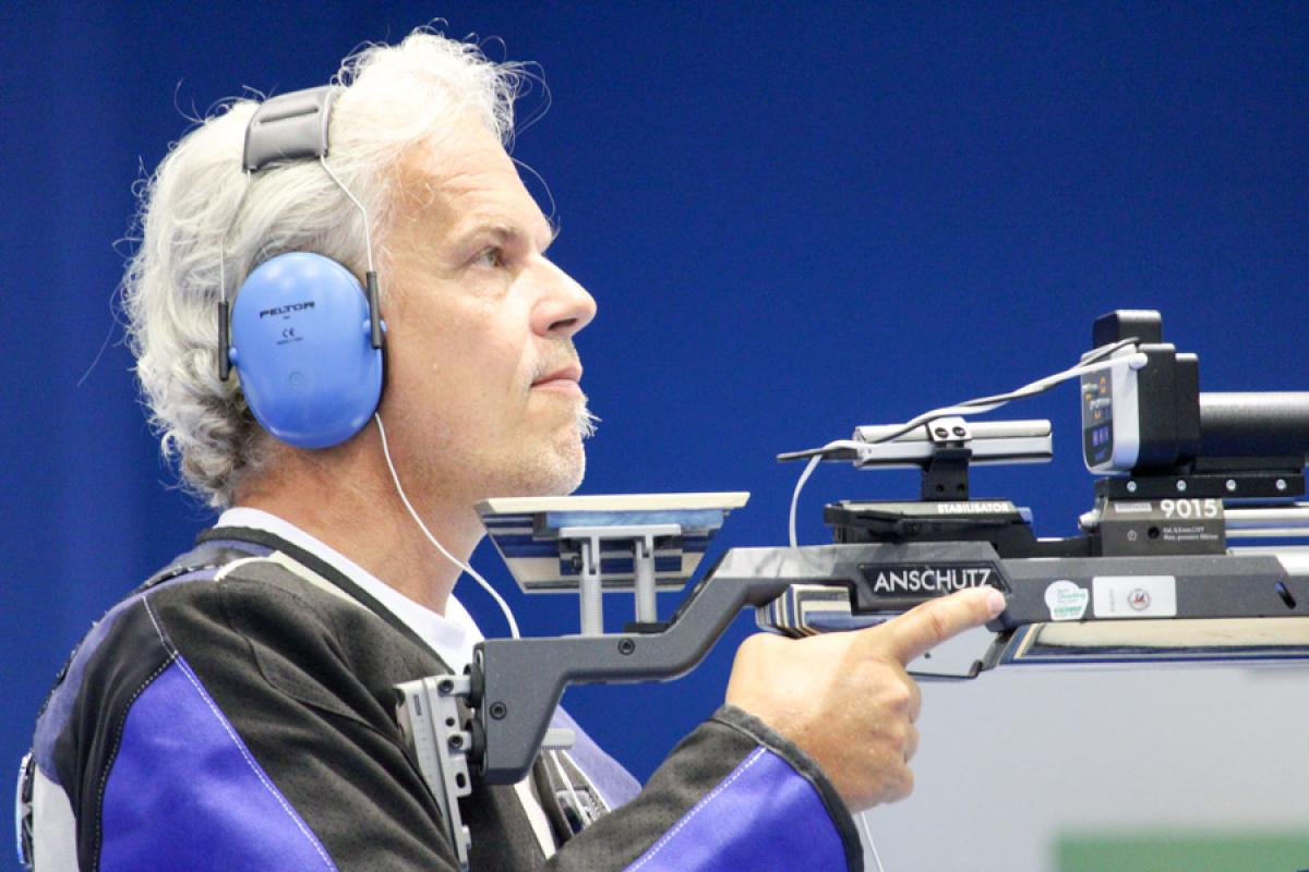 Male vision impaired rifle shooting athlete looks on with noise canceling ear protectors on