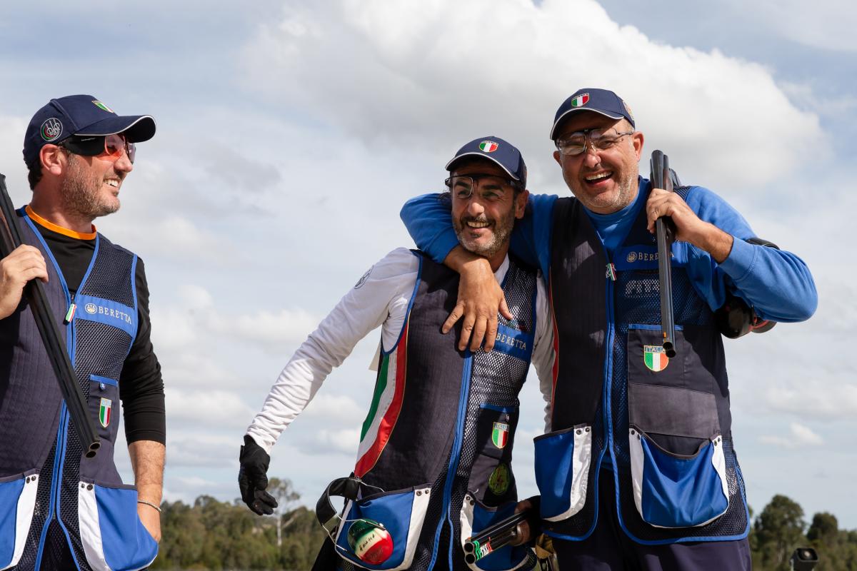 Two Italian shotgun athletes have arms around each other laughing 