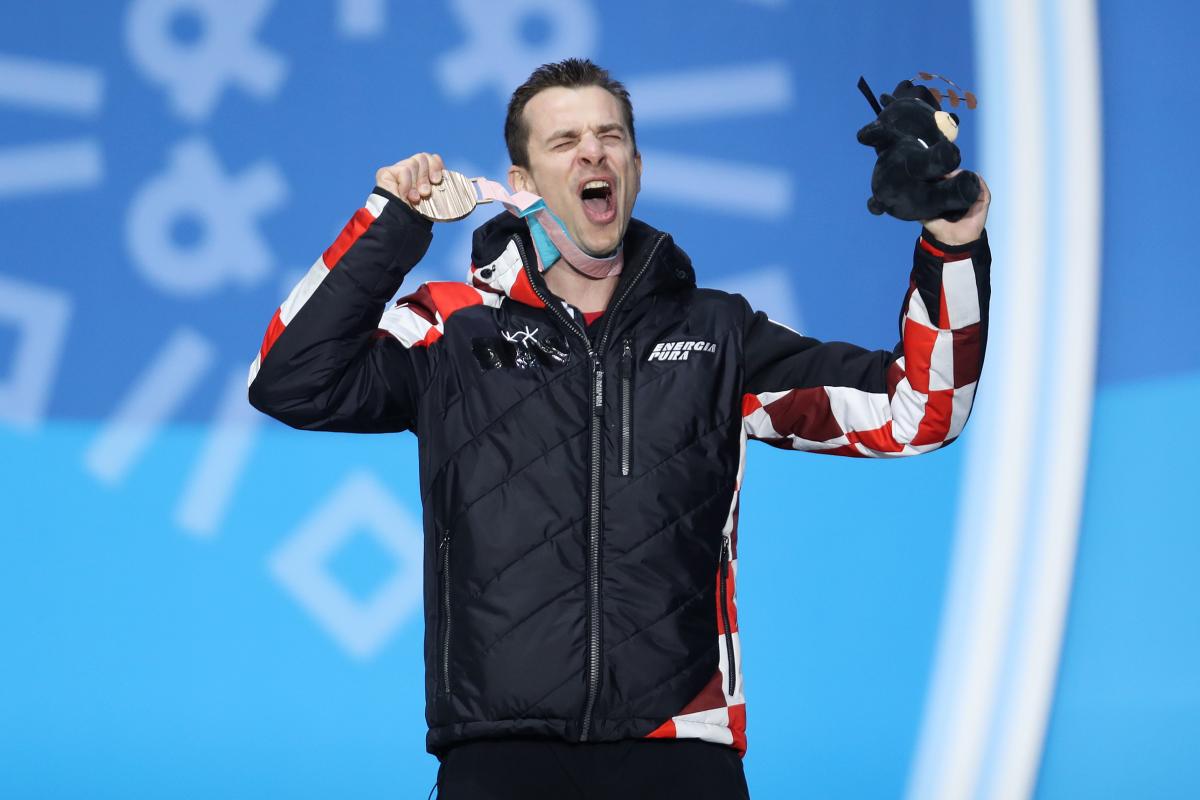 A man celebrating and showing his bronze medal on the podium 