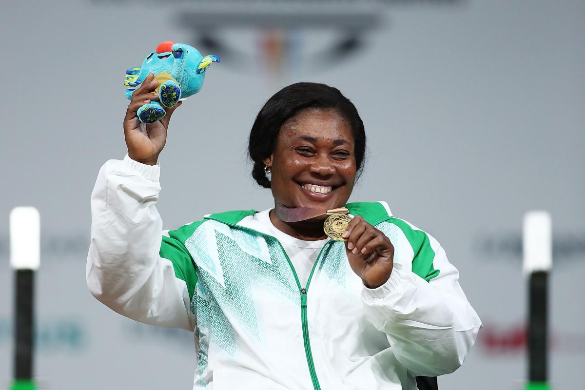 A woman holding a mascot with the right hand and showing the medal with her left hand