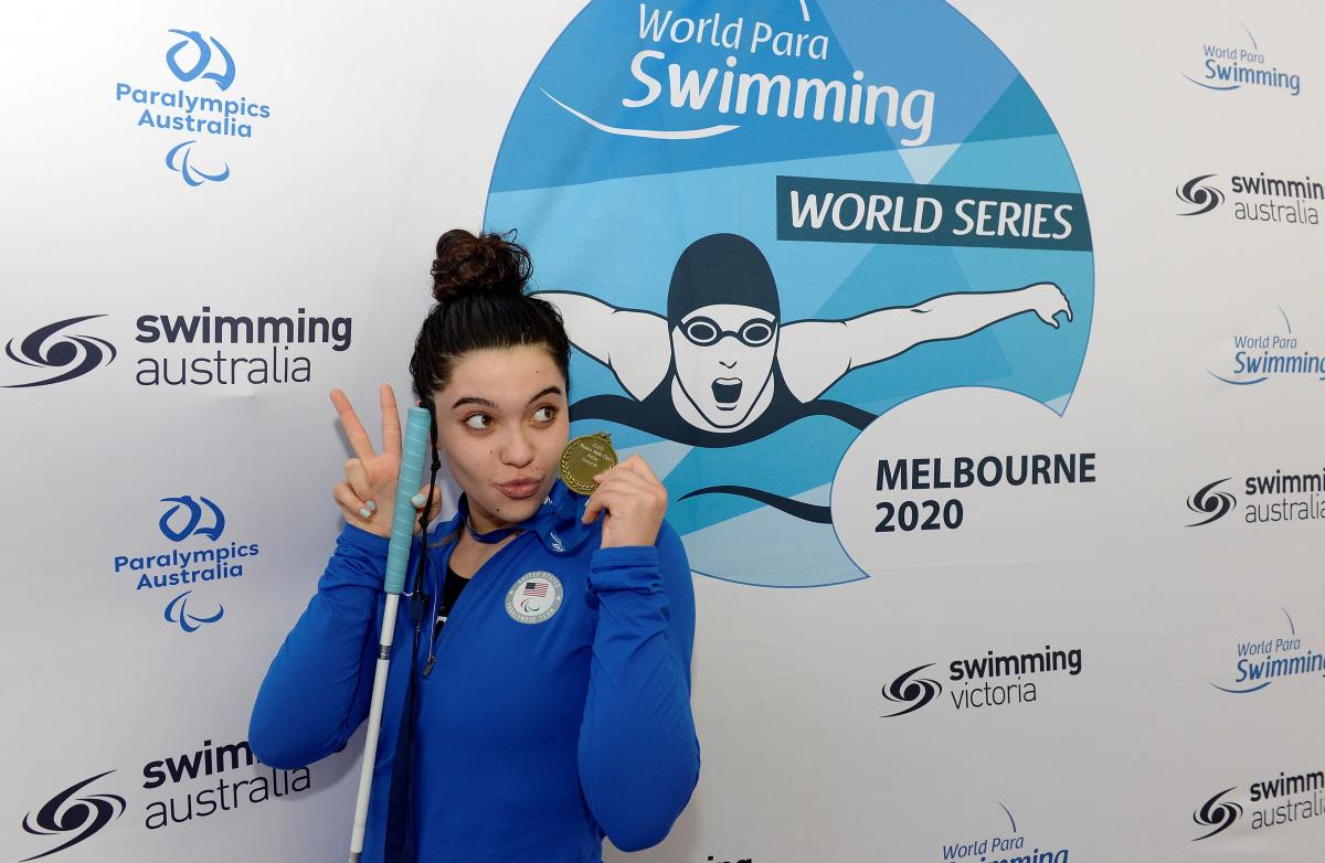 A teenage girl holding a cane and a gold medal while posing for a photo