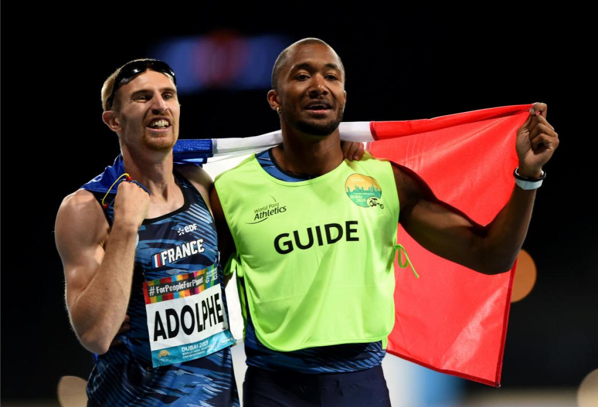 A white vision impaired man and his guide celebrate holding the French flag