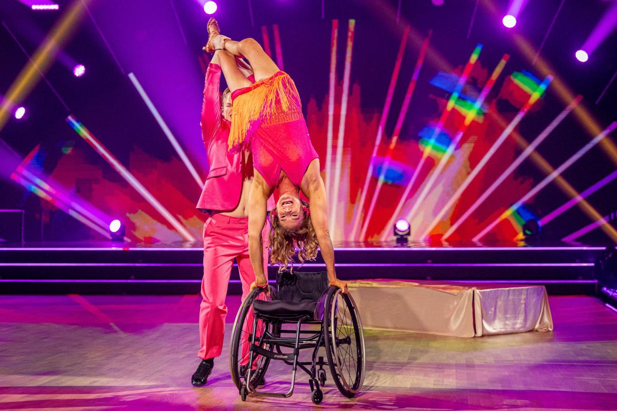 A woman in a wheelchair on a dance floor held by her dance partner