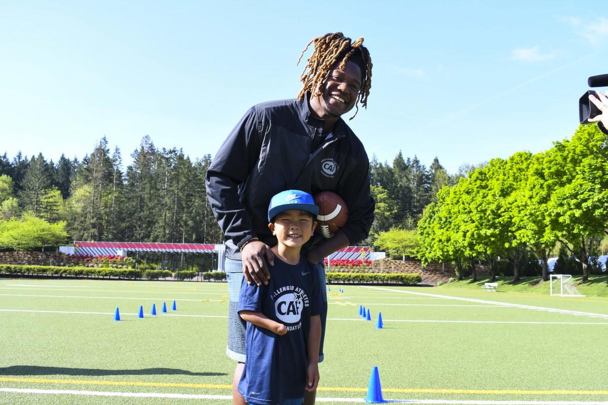 Black male athlete holding an American football and smiling with a kid with an arm impairment