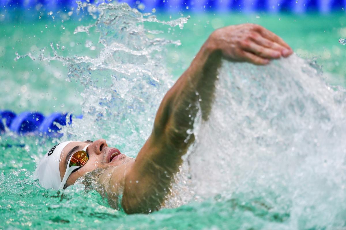 A man with a white cap swimming backstroke in a swimming pool