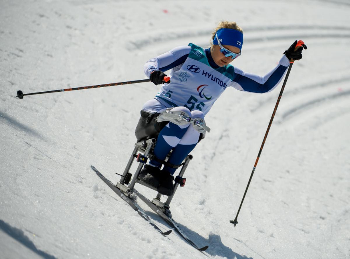 A female sit-skier with a bandana with the flag of Finland competing in cross-country skiing