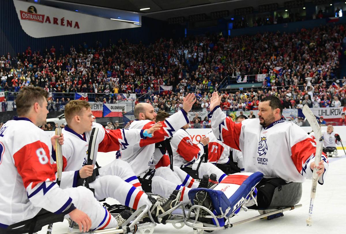 One Para ice hockey player giving high five to a group of players on sledges in a crowded ice hockey arena