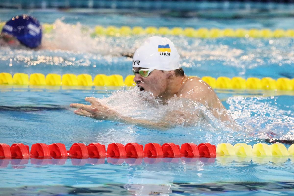 A man with a white cap and the Ukrainian flag swimming breaststroke in a pool