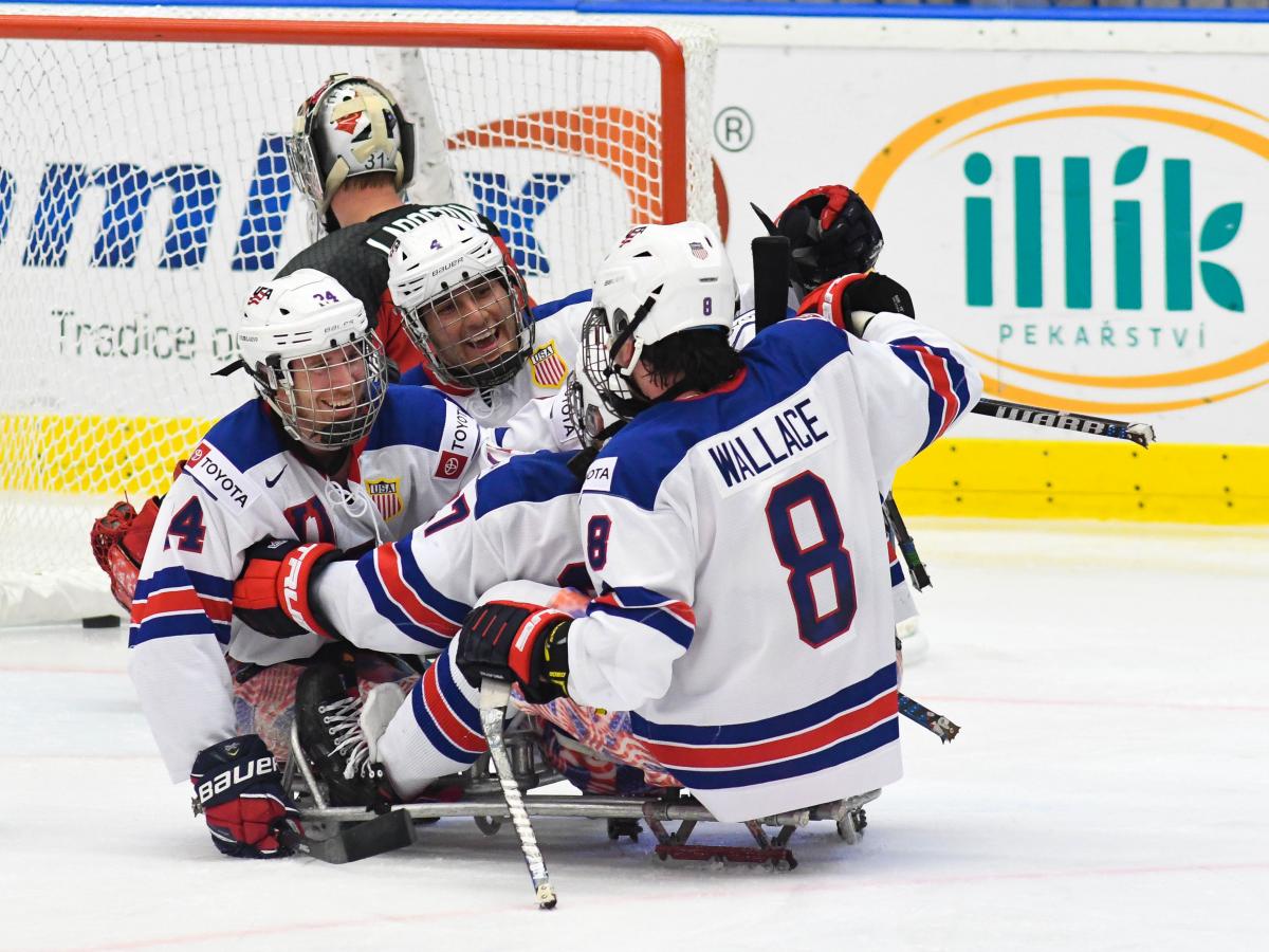 Three USA Para ice hockey players hugging during a game on an ice rink