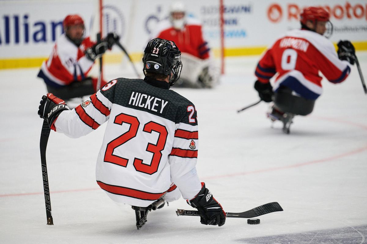 A Para ice hockey player seen from behind in a match observed by three players