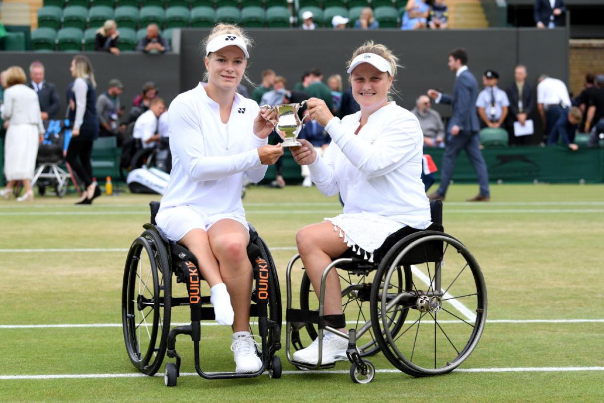 Two women in wheelchairs holding Wimbledon trophy together