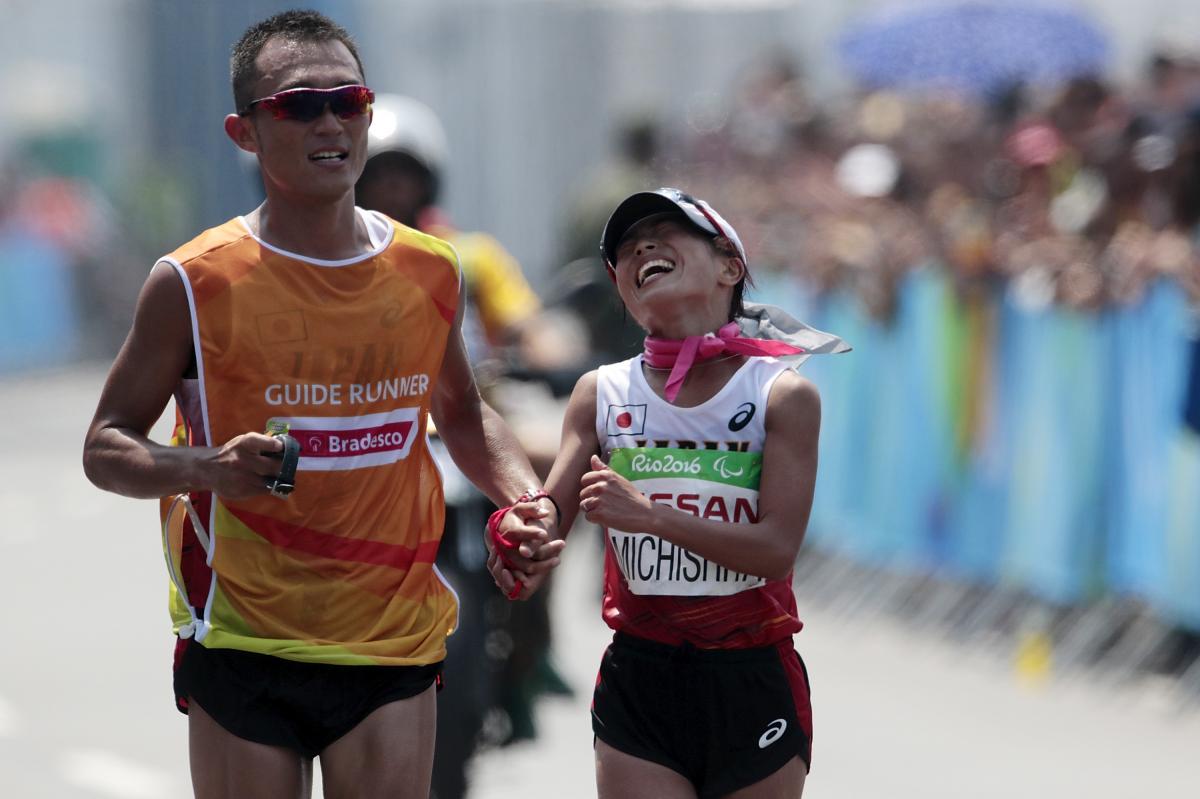 A woman running right next to a male runner guide during a marathon on a street